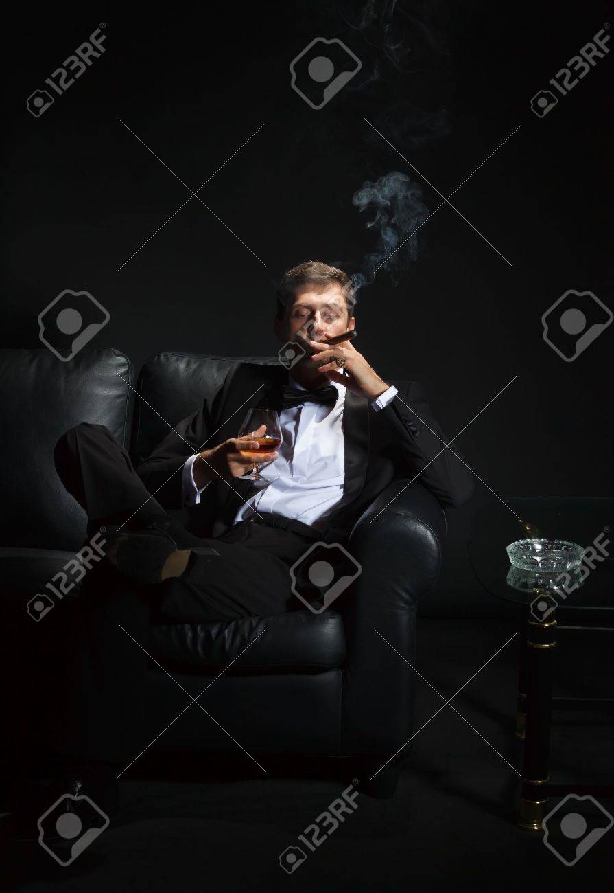 15896974-Macho-man-in-a-stylish-tuxedo-sitting-in-the-darkness-at-a-nightclub-puffing-on-a-cigar-and-drinking-Stock-Photo.jpg