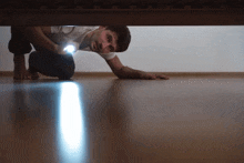 a man crawls under a bed holding a flashlight